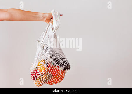 Woman's hand holding un sac réutilisable plein de légumes du marché sur le mur blanc Banque D'Images