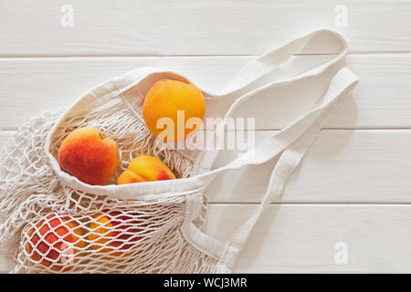 Pêches mûres fraîches du marché d'agriculteurs dans une chaîne sac réutilisable sur la table en bois blanc Banque D'Images