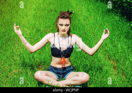 Cosplay girl maquillage agressif Viking dans un champ de blé vert. À genoux, priant pour les anciens dieux. Le Paganisme, le féminisme, l'indépendance, la tribu. Banque D'Images