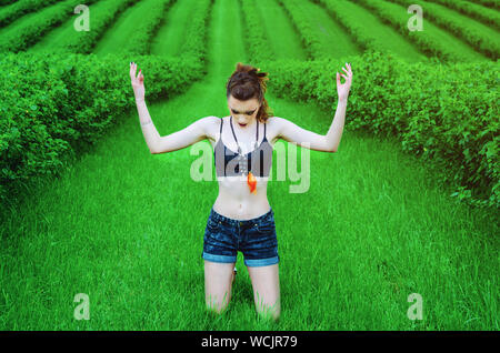 Cosplay girl maquillage agressif Viking dans un champ de blé vert. À genoux, priant pour les anciens dieux. Le Paganisme, le féminisme, l'indépendance, la tribu. Banque D'Images