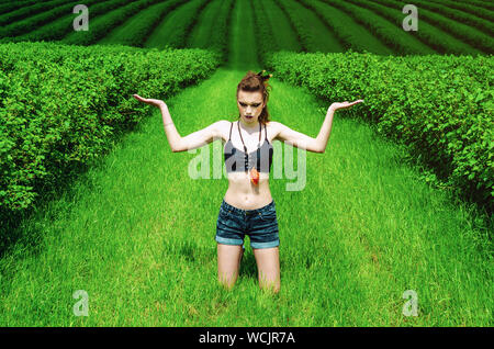 Cosplay girl maquillage agressif Viking dans un champ de blé vert. À genoux, priant pour les anciens dieux. Le Paganisme, le féminisme, l'indépendance, la tribu. Banque D'Images