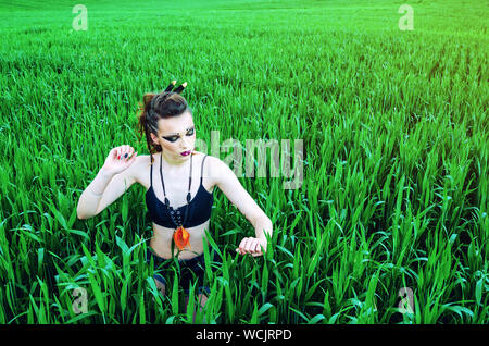 Fille maquillage agressif, amazon caractère dans un champ de blé vert. Féminisme, indépendance, tribu. Banque D'Images