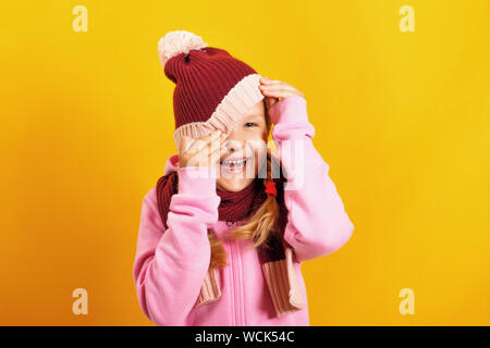 Portrait d'une petite fille dans une écharpe et noir sur un fond jaune. L'enfant de pics de sous le chapeau. Banque D'Images