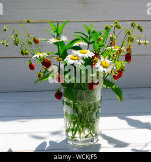 Branches de fraise mûre, rouge, blanc les marguerites et les feuilles de menthe dans un verre d'eau sur un moignon de bois Banque D'Images