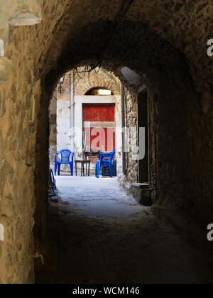 Ruelle étroite dans village médiéval de Mesta sur l'île de Chios, Grèce. Table et chaises en plastique bleu. Banque D'Images