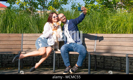 L'heureux couple sont assis sur le banc dans le parc et un petit chien et ne portrait selfies. Corgi Pembroke mignon chiot sur ses propriétaires les mains. Concepts Banque D'Images