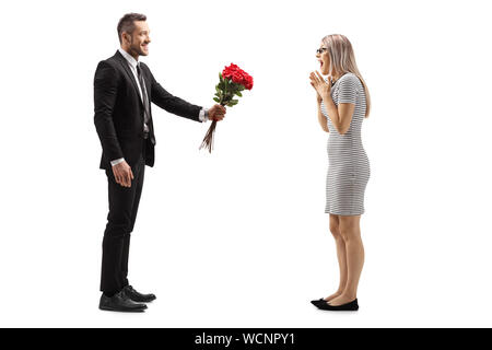 Profil de pleine longueur de balle un jeune homme souriant et donnant un bouquet de roses rouges à une femme surprise isolé sur fond blanc Banque D'Images