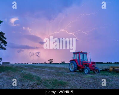 Foudre fourchue sur tracteurs garés dans un champ pendant un orage d'été, période tumultueuse de l'avant pour les agriculteurs britanniques Banque D'Images