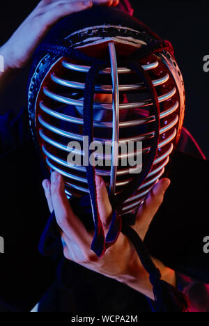 Close up shot, le Kendo fighter port d'une armure et lie les kimonos traditionnels le laçage sur son casque debout sur un fond noir. Banque D'Images