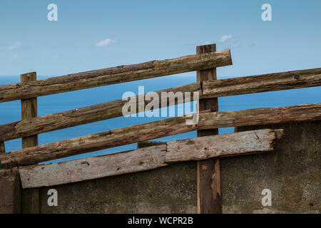 Clôture en bois avec base en béton autour de la zone agricole sur une colline. L'eau bleu de l'océan Atlantique à l'arrière-plan. Des nuages blancs. Sao Miguel, Açores, Banque D'Images