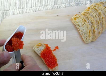 Préparation des sandwichs avec du caviar rouge. Caviar de saumon rouge est enduite avec un couteau de cuisine sur une tranche de pain blanc. De délicieuses spécialités culinaires. Banque D'Images