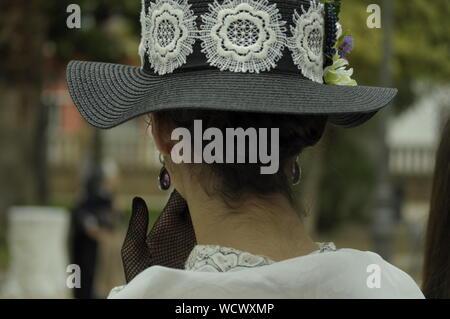 Jeune femme portant des vêtements de style moderniste, avec sa main sur sa bouche. Portant un grand chapeau avec des fleurs et des gants. Femme élégante portant des vêtements vintage Banque D'Images