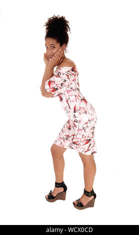 Une magnifique jeune femme multi-raciale debout dans une robe d'été de profil, avec ses mains sur son visage et cheveux noirs frisés en chignon, isolée pour whit Banque D'Images