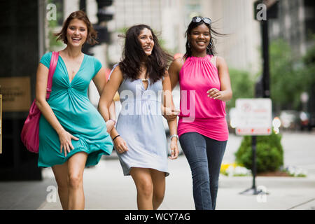 Trois female friends walking avec bras reliés le long d'une rue du centre-ville. Banque D'Images