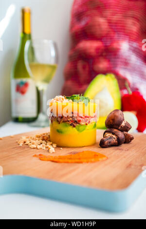 Plat péruvien, causa Limeña avec champignons grillés, avec un arrière-plan des ingrédients utilisés pour les réaliser et d'un verre de vin Banque D'Images