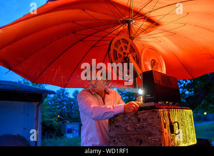 Waren, Allemagne. Août 28, 2019. Sous un parasol rouge, le 16mm projecteur est préparé par le musicien Gunthard Stephan pour la projection de divers films muets. Voyager avec leur cinéma, un ancien pompier Magirus Deutz construit en 1969, les deux musiciens étudiés voyager dans toute l'Allemagne. Tous les genres de films muets sont indiquées - à partir de leur création en 1895 à la fin de l'époque du film muet autour de 1930. Credit : Jens Büttner/dpa-Zentralbild/dpa/Alamy Live News Banque D'Images