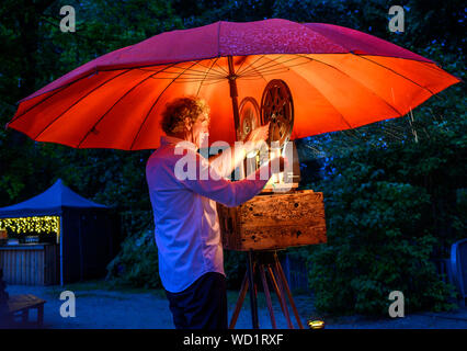 Waren, Allemagne. Août 28, 2019. Sous un parasol rouge, le 16mm projecteur est préparé par le musicien Gunthard Stephan pour la projection de divers films muets. Voyager avec leur cinéma, un ancien pompier Magirus Deutz construit en 1969, les deux musiciens étudiés voyager dans toute l'Allemagne. Tous les genres de films muets sont indiquées - à partir de leur création en 1895 à la fin de l'époque du film muet autour de 1930. Credit : Jens Büttner/dpa-Zentralbild/dpa/Alamy Live News Banque D'Images