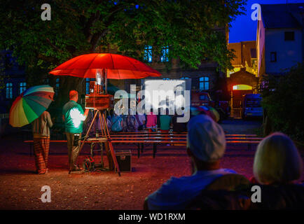 Waren, Allemagne. Août 28, 2019. Sous un parasol rouge, le 16mm projecteur est protégé de la pluie tandis que le rang des musiciens (piano) et Stephan (violon) Jouez en direct à l'écran différents films muets. Voyager avec leur cinéma, un ancien pompier Magirus Deutz construit en 1969, les deux musiciens étudiés voyager dans toute l'Allemagne. Tous les genres de films muets sont indiquées - à partir de leur création en 1895 à la fin de l'époque du film muet autour de 1930. Credit : Jens Büttner/dpa-Zentralbild/dpa/Alamy Live News Banque D'Images