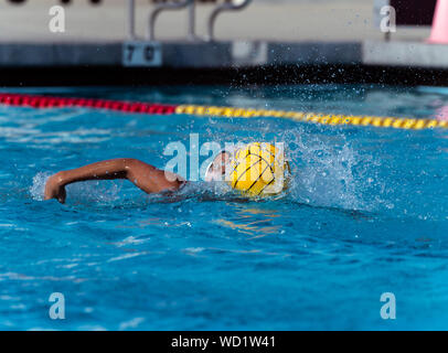 Joueur de water-polo en uniforme blanc se déplace et pousse la balle pour le côté offensif de piscine pendant que les projections d'eau. Banque D'Images