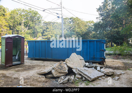 L'enlèvement des débris de démolition de bâtiments avec des déchets de construction et de gravats de béton rock on portable bio toilettes cabines sur le site de construction Banque D'Images