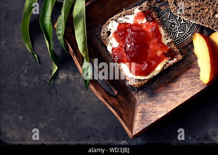 Brown tranche de pain complet avec du beurre et de la marmelade de fraises servi sur le plateau en bois rustique pour le petit-déjeuner. Vue de dessus, les simulacres de l'espace. Banque D'Images