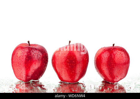 Trois pommes rouges en gouttes d'eau sur un miroir blanc avec fond isolé réflexion close up Banque D'Images