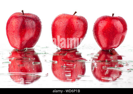 Trois pommes rouges en gouttes d'eau sur un miroir blanc avec fond isolé réflexion close up Banque D'Images