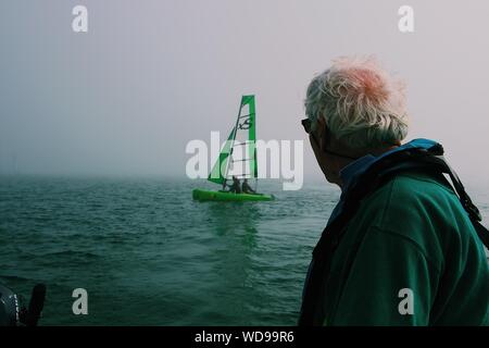 Gros plan d'un vieil homme en regardant un vert voilier sur le corps de l'eau Banque D'Images