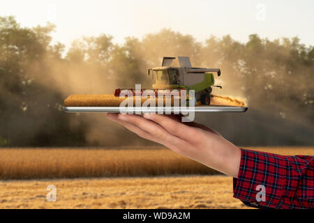 Farmer holding a tablet avec une moissonneuse-batteuse. La réalité augmentée et la transformation numérique dans l'agriculture. Concept d'agriculture intelligente Banque D'Images