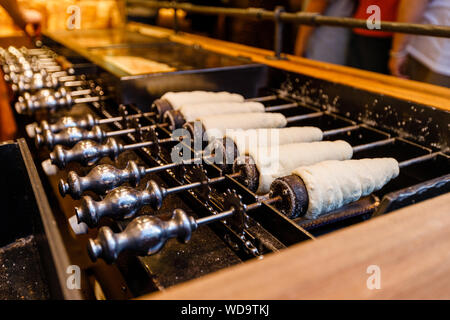 Préparation de la traditionnelle une sorte de Trdelník le champagne fait à partir de pâte roulée enroulé autour d'un bâton, grillé Banque D'Images