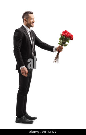 Profil de pleine longueur de balle un jeune homme élégant de sourire et de donner un bouquet de roses rouges isolé sur fond blanc Banque D'Images