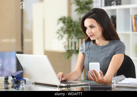 Employée de bureau travaillant sur la ligne à l'aide de smart phone et l'ordinateur portable sur un bureau Banque D'Images