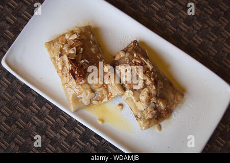 Crêpes russes avec du fromage cottage et de remplissage des amandes tranchées et de miel sur le dessus. Délicieux dessert sur la plaque blanche. Banque D'Images