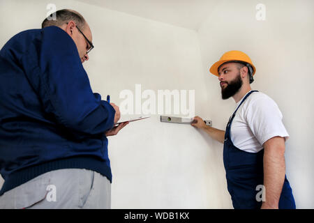 L'ingénieur, l'entrepreneur et le chef de projet avec son collègue, travailleur de la construction, d'un bricoleur et builder est la mesure de mur à l'aide d'un niveau à l'outil. Banque D'Images