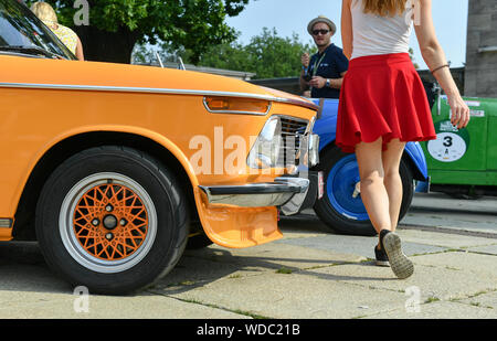 29 août 2019, Berlin : Une femme avec une jupe rouge passe oldtimers de couleur au début du rallye de voitures classiques 'Hamburg-Berlin-Klassik" au Stade Olympique. Le rallye commence à le Stade Olympique de Berlin et mène à travers le Mecklembourg Lake District à Hambourg et à l'Émigration Museum. Photo : Jens Kalaene Zentralbild-/dpa/afp Banque D'Images