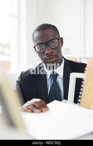 Portrait de l'employé de bureau de graves dans les lunettes et costume looking at camera tout en faisant le travail de bureau Banque D'Images