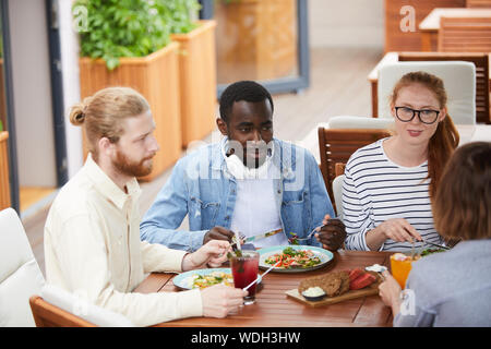 Groupe de jeunes multiethniques assis à la table et de parler les uns aux autres pendant que le déjeuner au restaurant Banque D'Images