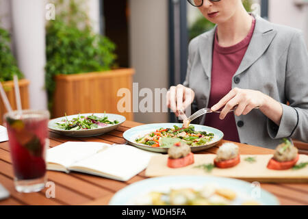 Close-up de jeune femme assise à la table et de manger une salade de légumes au cours de son dîner d'affaires en outdoor cafe Banque D'Images