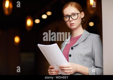 Portrait de jeune femme aux cheveux rouges lunettes dans les documents d'affaires et de portefeuille looking at camera Banque D'Images