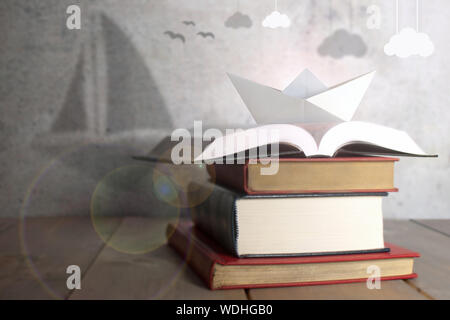 Bateau de papier sur le dessus d'une pile de livres par l'ombre d'un voilier avec nuages suspendus Banque D'Images