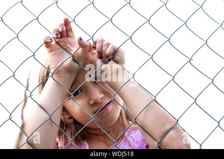 Sad girl derrière metal wire mesh fence. Enfant solitaire et abandonnée à l'extérieur. Déprimé preteen aux yeux clos tenant la cage d'acier chaîne. Loneline Banque D'Images