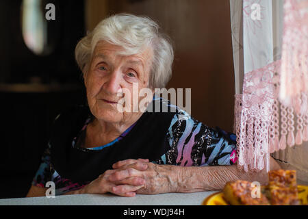 Vieille dame aux cheveux gris portrait en gros à la table de la cuisine. Banque D'Images