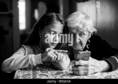 Cute little girl montre son arrière grand-mère d'un smartphone. Photo en noir et blanc. Banque D'Images