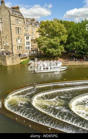 BATH, ANGLETERRE - Juillet 2019 : en forme de fer à cheval Le Pulteney Weir sur la rivière Avon, dans le centre de Bath. Un bateau de tourisme est en arrière-plan. Banque D'Images