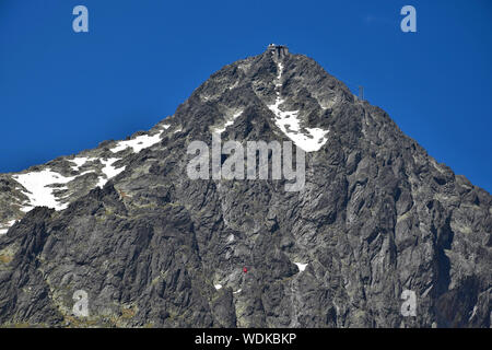 Lomnicky Stit dans les Tatras. Le téléphérique rouge sur son chemin vers le sommet est minuscule en face de la montagne. Banque D'Images