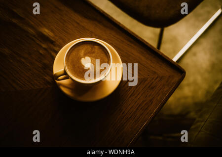 Cappuccino avec coeur en jaune tasse et la plaque de ci-dessus. Effet de filtre aux teintes chaleureuses. Banque D'Images