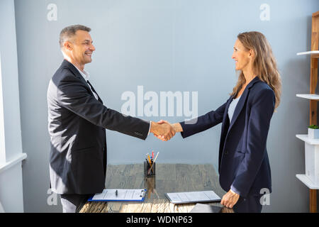 Vue latérale du Smiling Mature Businessman Shaking Hands With His In Office Banque D'Images