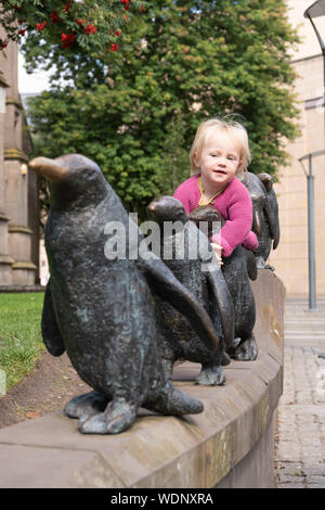 Un bambin épouse l'un des cinq pingouins dans la sculpture par Angela Hunter près du centre commercial Overgate à Dundee Banque D'Images