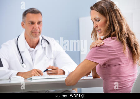 Médecin à la femme mature au patient en montrant son épaule peinture en clinique Banque D'Images