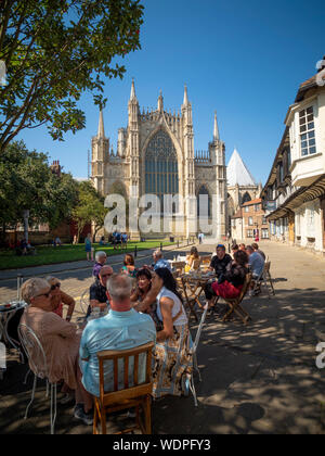 Les gens assis dehors au café avec York Minster et St Williams College en arrière-plan, la rue College, York, Royaume-Uni. Banque D'Images